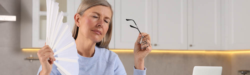 Middle aged woman experiencing hot flashes and fanning herself Middle aged woman experiencing hot flashes and fanning herself